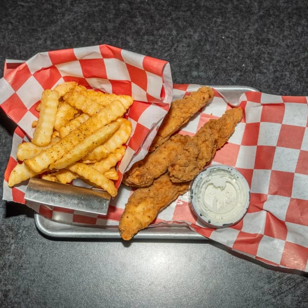 A metal tray holds crispy chicken tenders, seasoned crinkle-cut fries, and a side of ranch dressing.
