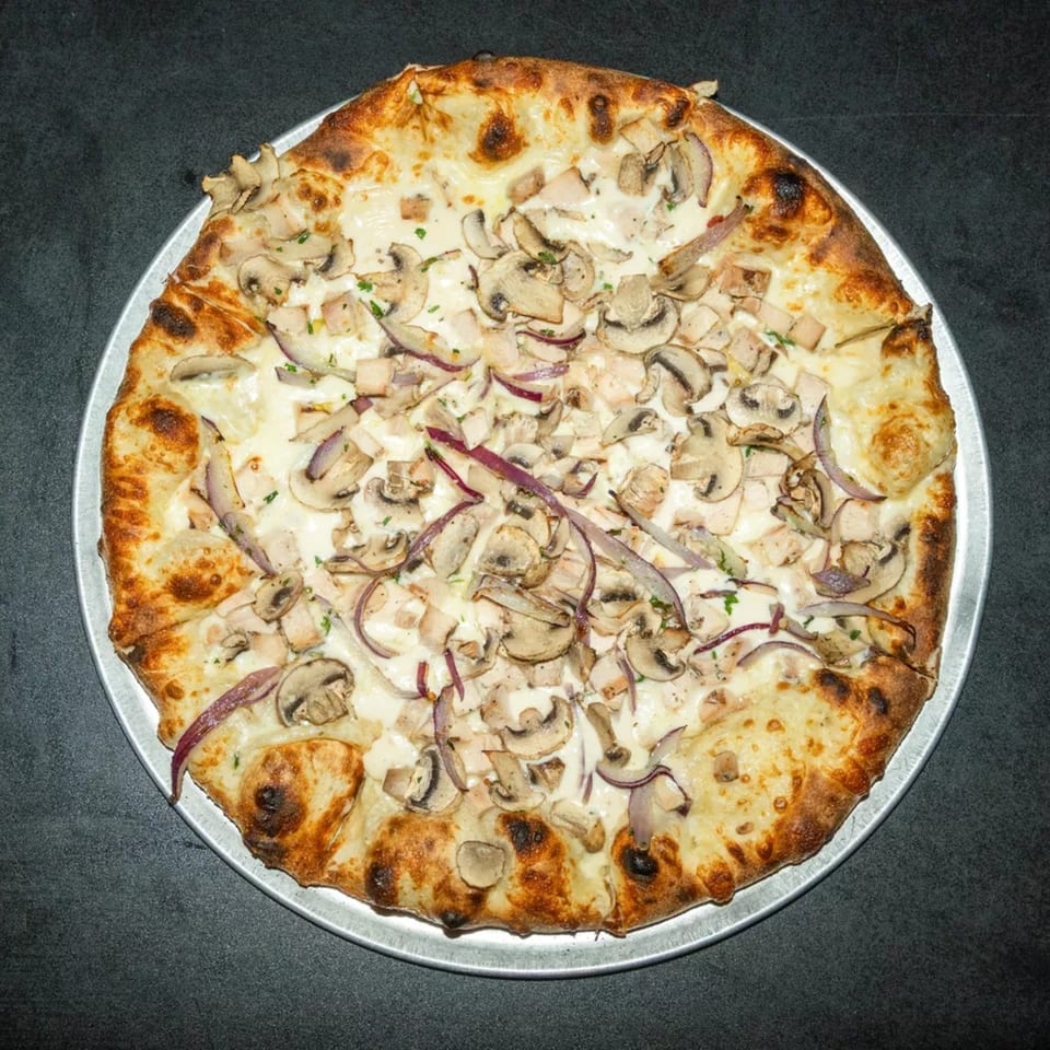 White pizza with chicken, mushrooms, and red onions on a metal tray.