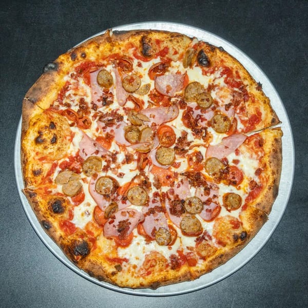 A whole meat lover's pizza with sausage, ham, and bacon on a metal pan.