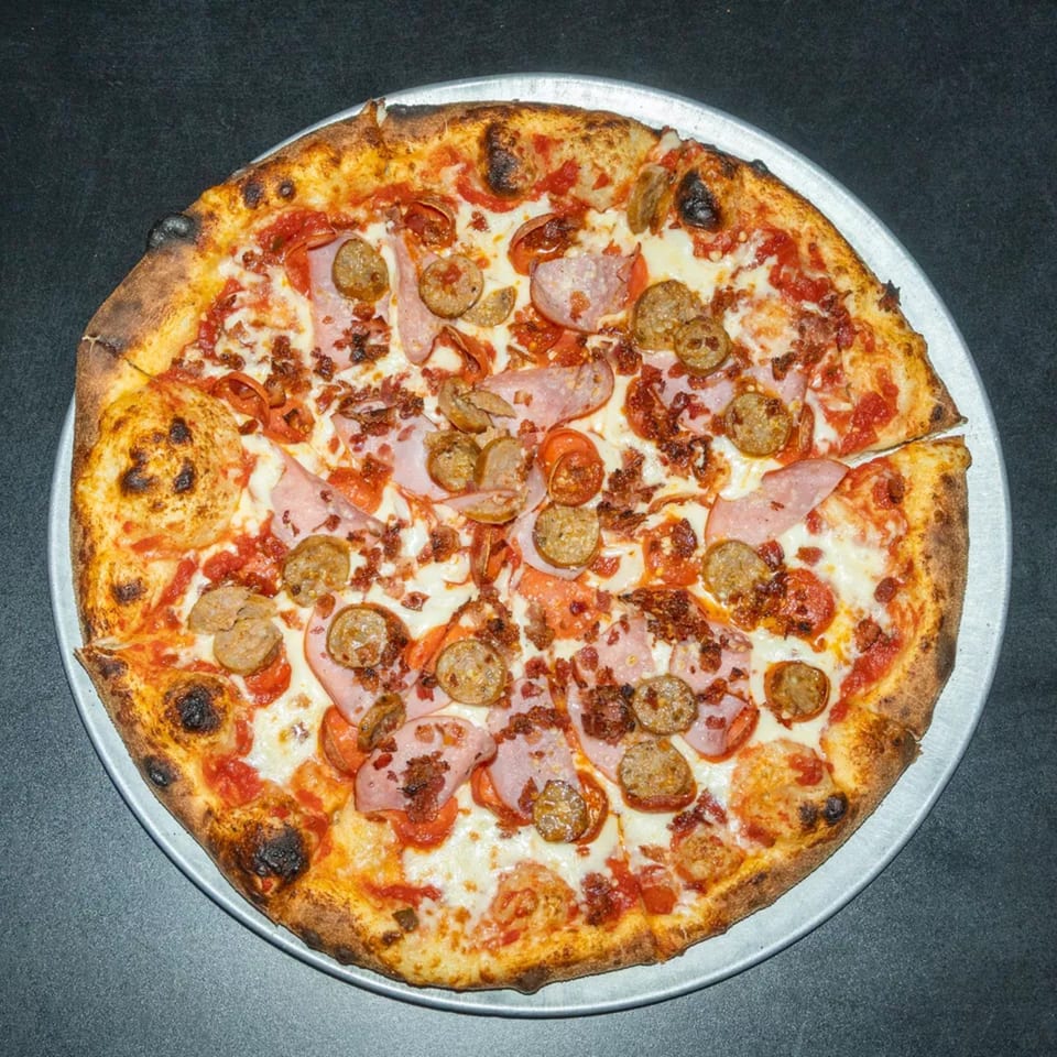 A whole meat lover's pizza with sausage, ham, and bacon on a metal pan.