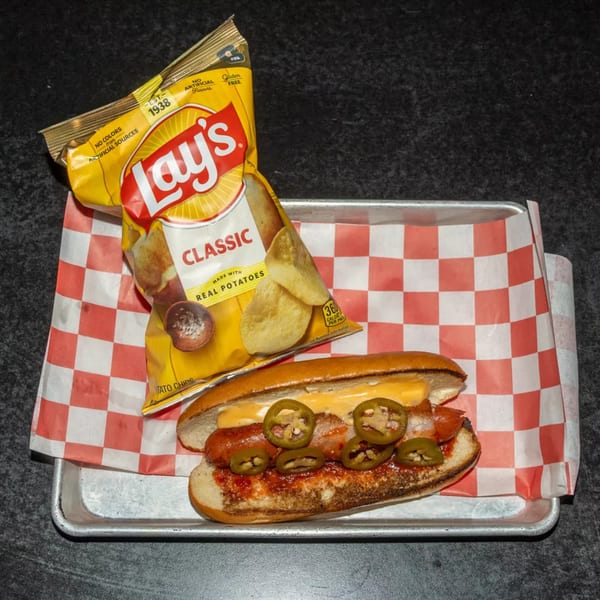 A hot dog with cheese and jalapeños, served with a bag of Lay's Classic potato chips.